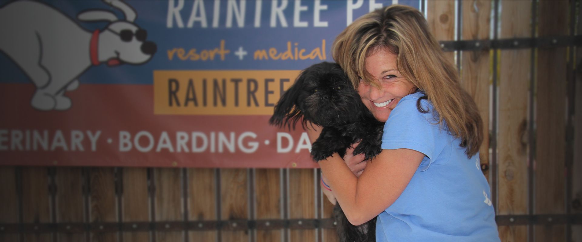 raintree pet employee hugging black furry dog